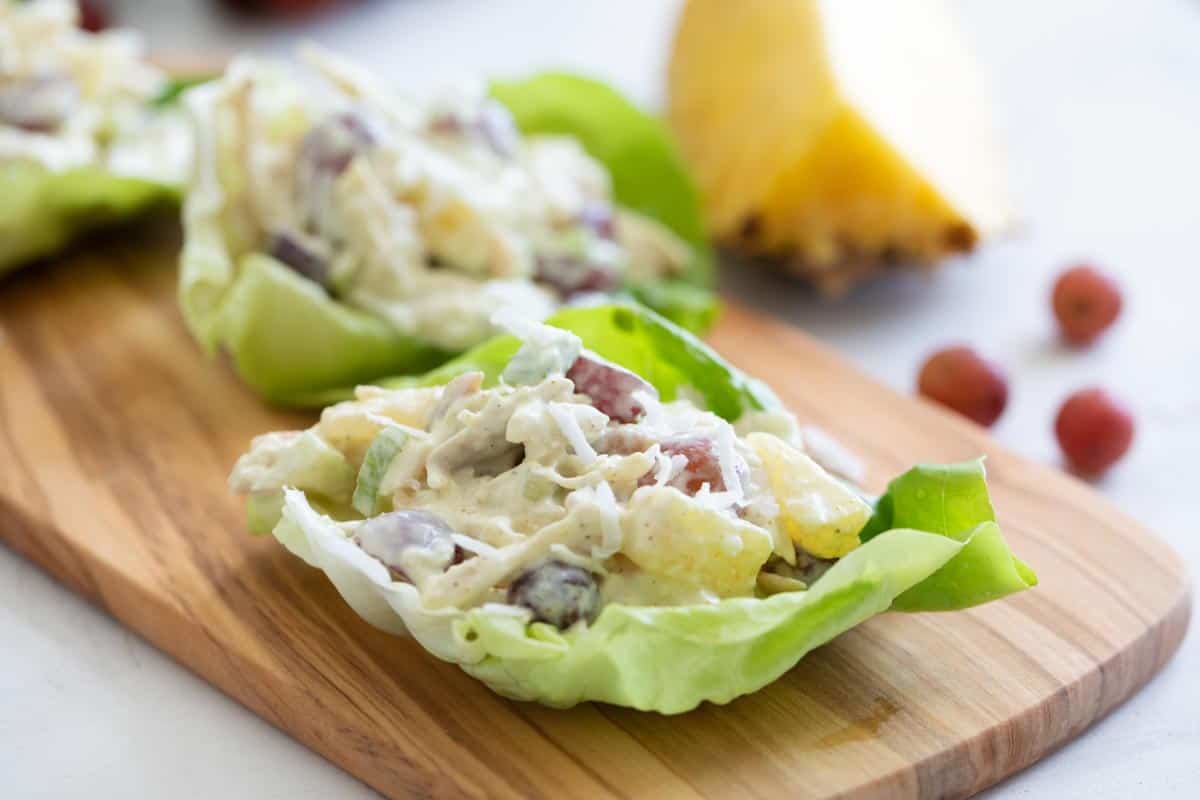 Chicken salad with an island twist - these Tropical Chicken Lettuce Wraps are filled with chicken, pineapple, grapes, and coconut with a creamy sauce to make the perfect lettuce wraps. chicken lettuce wraps with pineapple, grapes and coconut on a cutting board