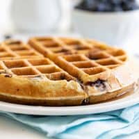 thick blueberry waffle on a white plate with syrup dripping