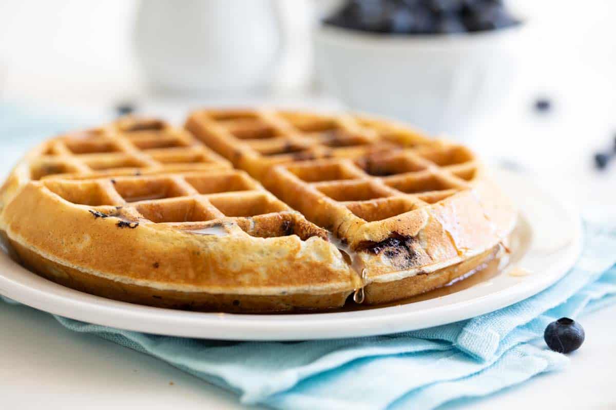 thick blueberry waffle on a white plate with syrup dripping