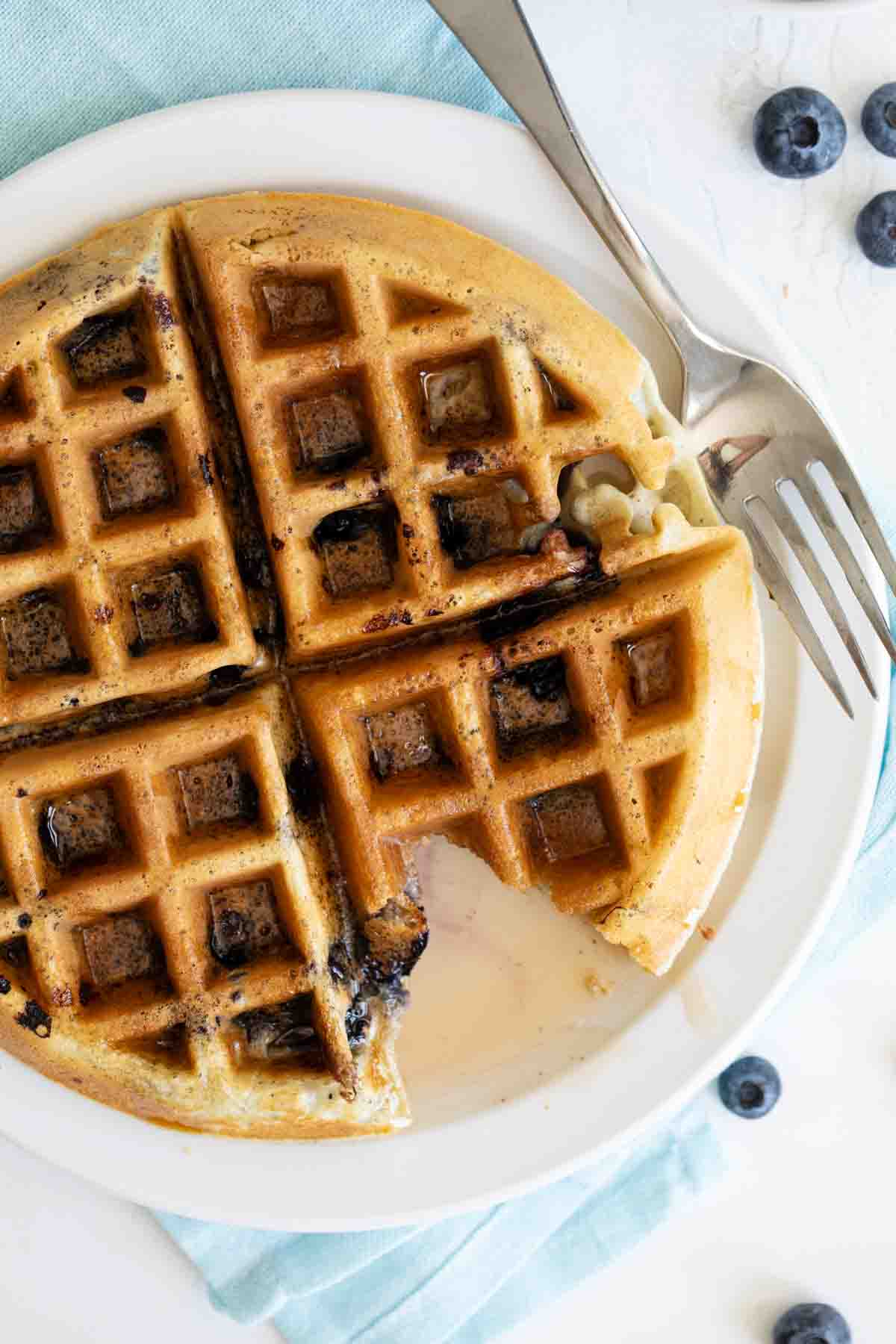 overhead view of blueberry waffle with syrup with a bite taken