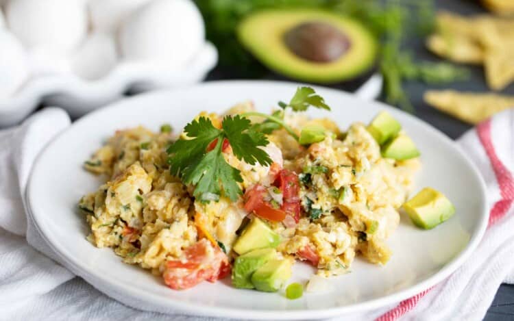 portion of migas on a plate topped with cilantro and avocado