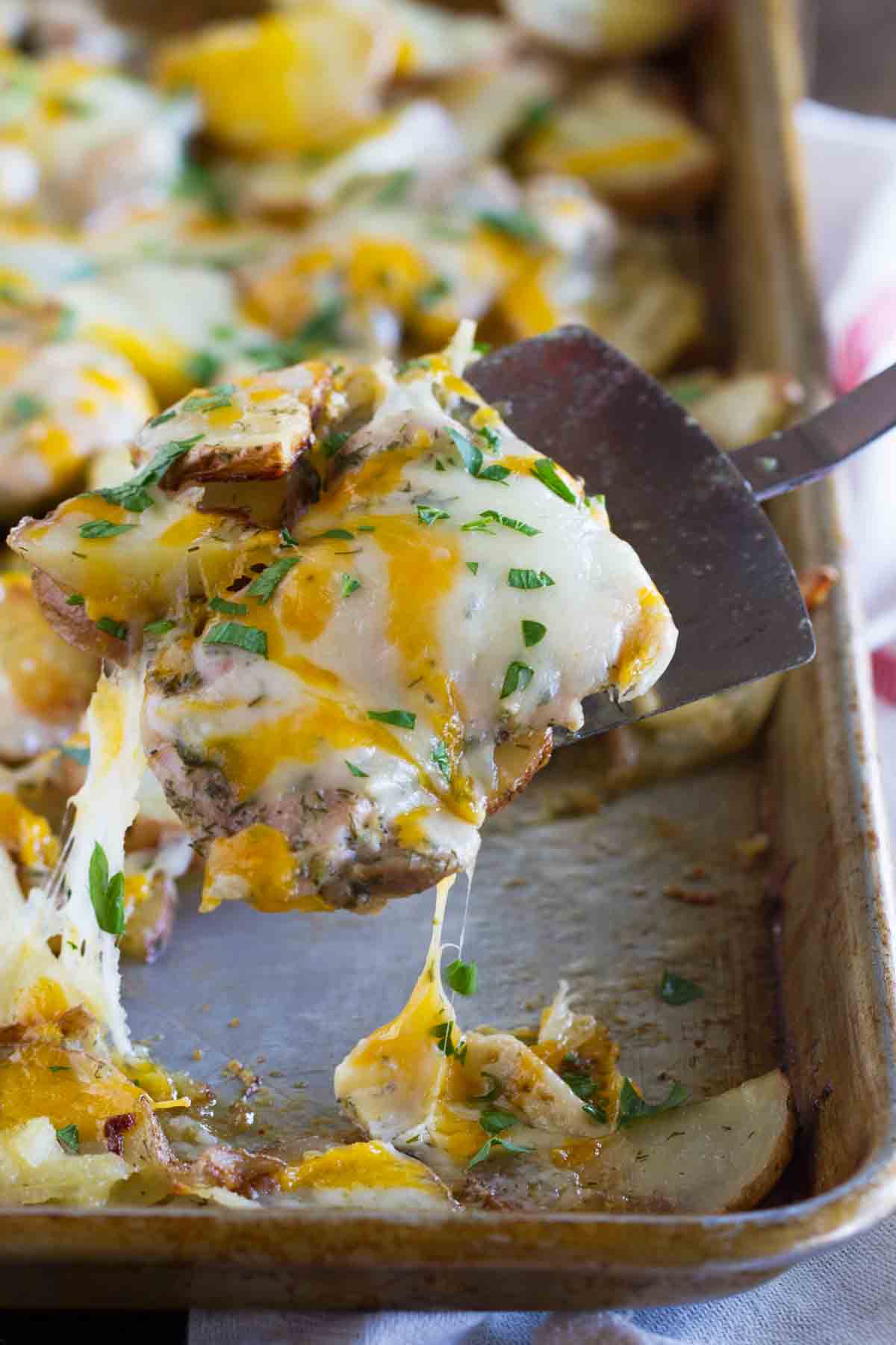 scooping chicken covered in cheese from a sheet pan