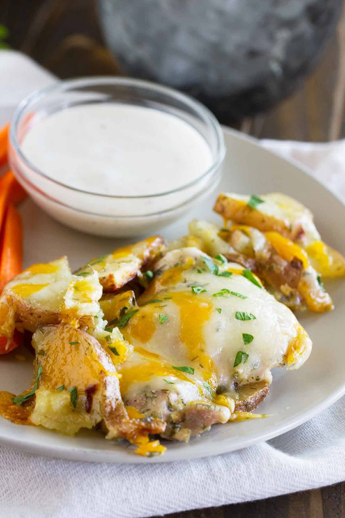 plate with ranch chicken and potatoes covered in cheese with ranch dressing for dipping