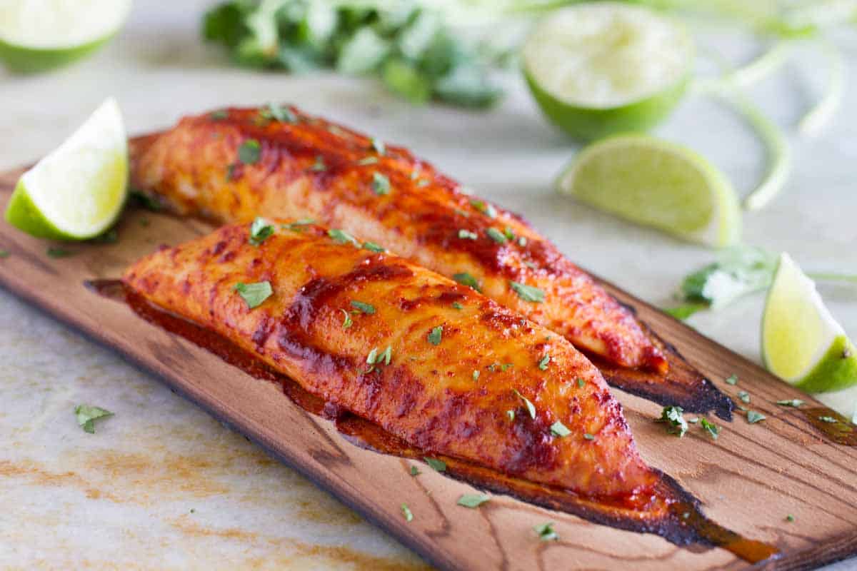 2 grilled fish filets on a cedar plank with lime wedges