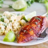 White plate with taco seasoned grilled fish, corn salad and lime wedges