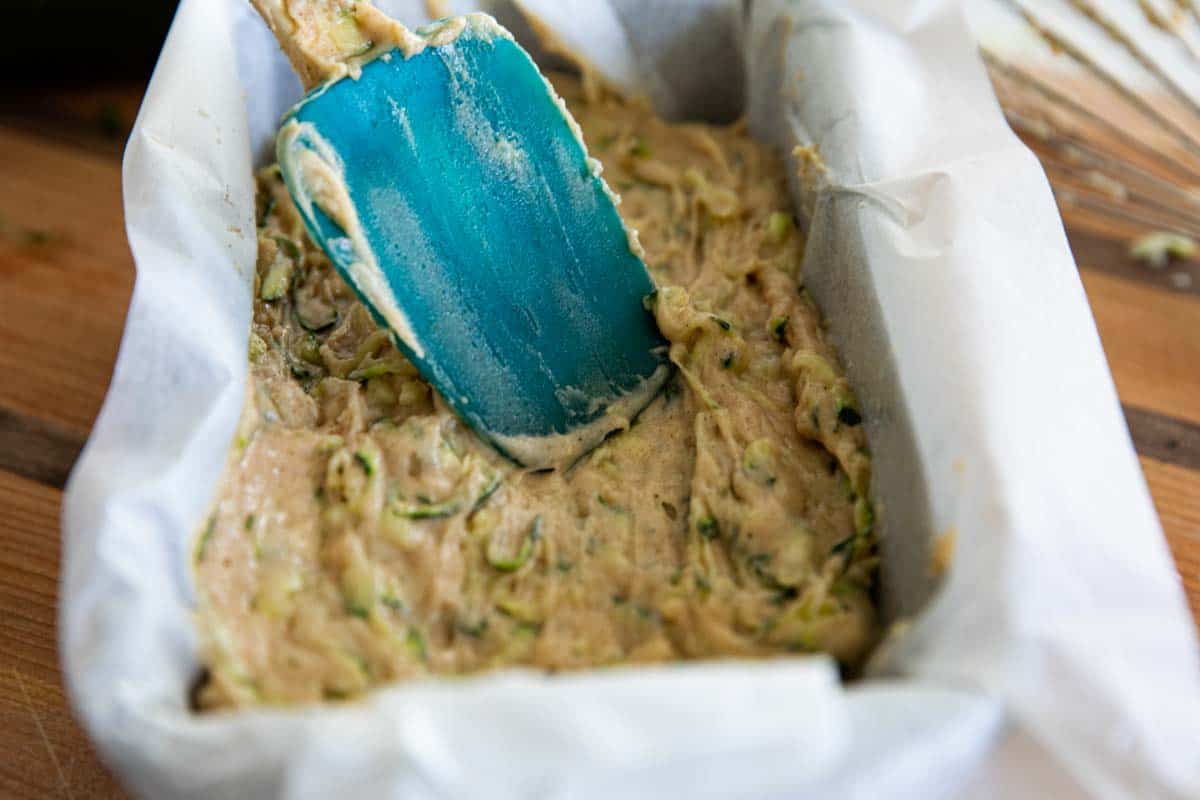 spreading zucchini bread batter into a parchment paper lined baking tin