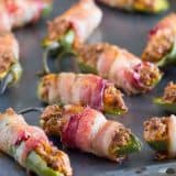 bacon wrapped jalapeno poppers with taco filling on a baking sheet