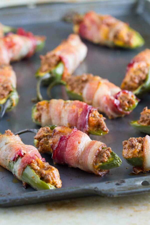 bacon wrapped jalapeno poppers with taco filling on a baking sheet
