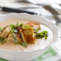 bowl of tomato soup topped with croutons and basil