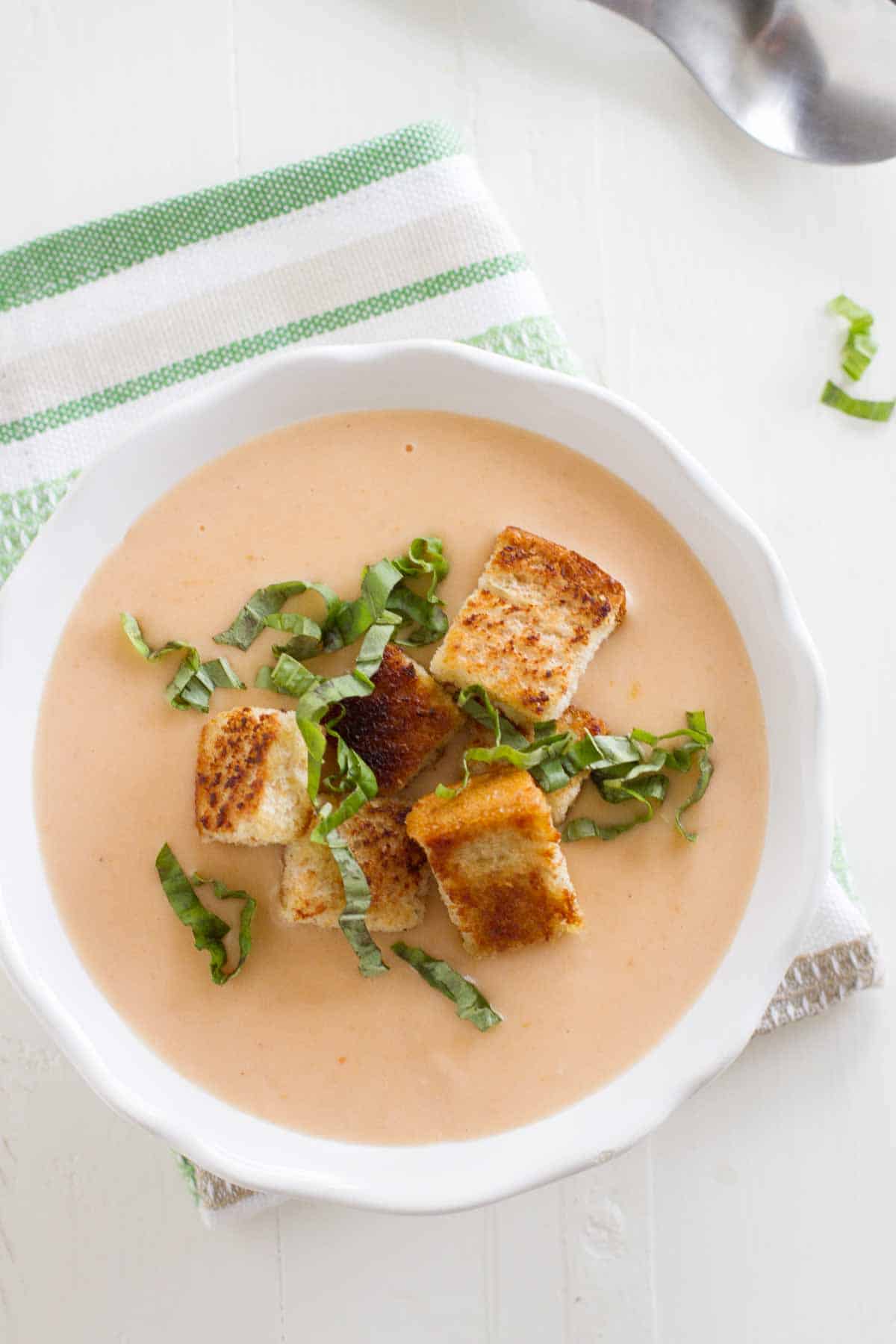overhead view of creamy tomato soup with homemade croutons and basil