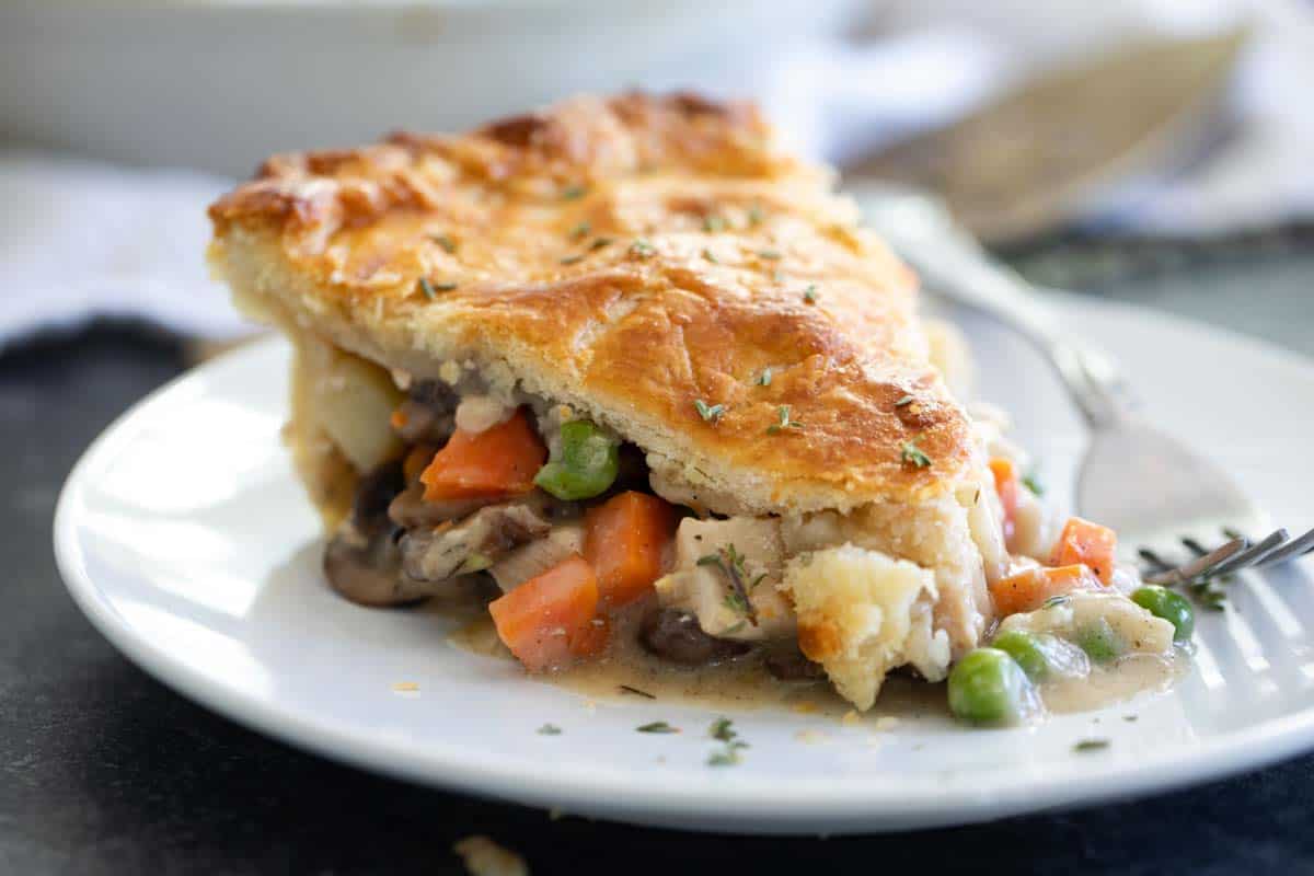 It doesn’t get more comforting than this homemade Chicken Pot Pie recipe! Tender chicken and vegetables are combined with a homemade gravy and baked between two flaky pie crusts. slice of chicken pot pie on a plate