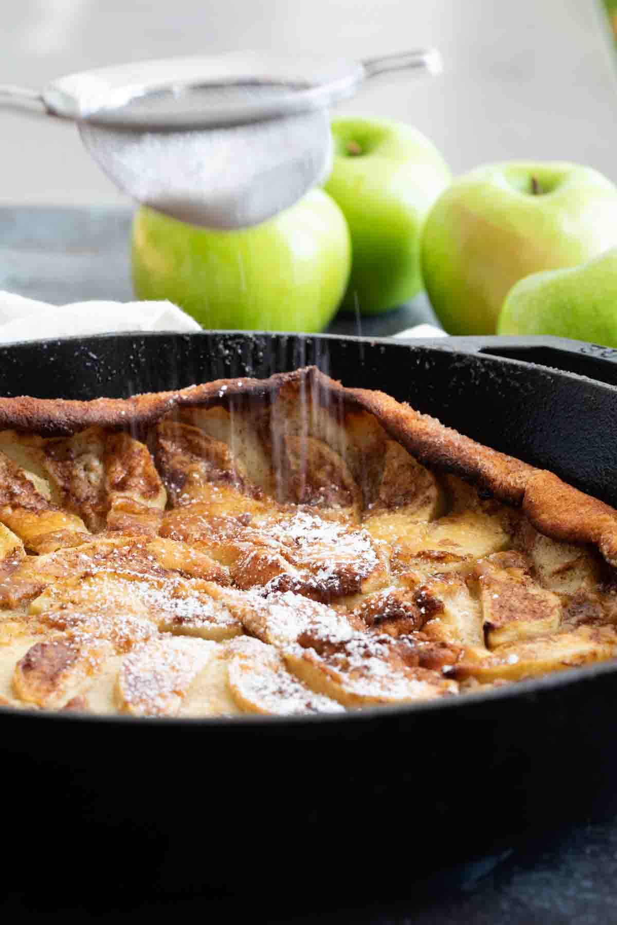 shaking powdered sugar onto a German Apple Pancake