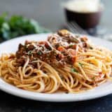 plate with pasta and bolognese topped with parsley and cheese