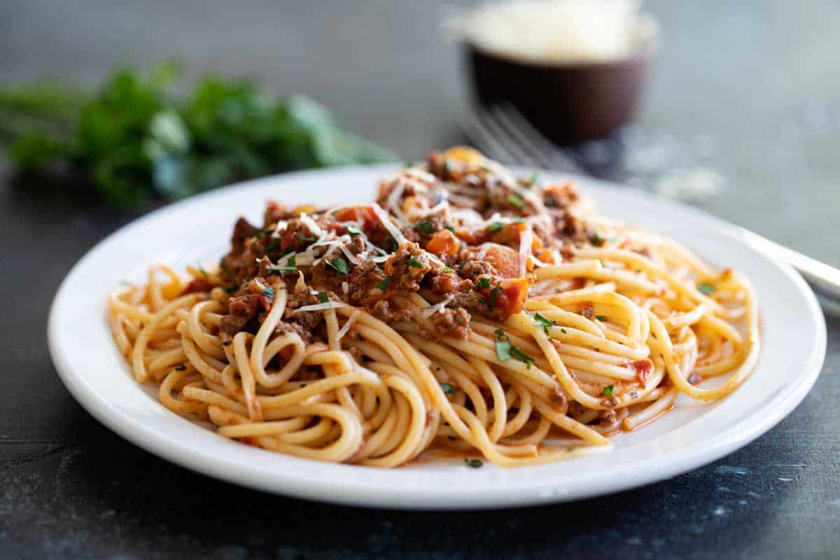 plate with pasta and bolognese topped with parsley and cheese