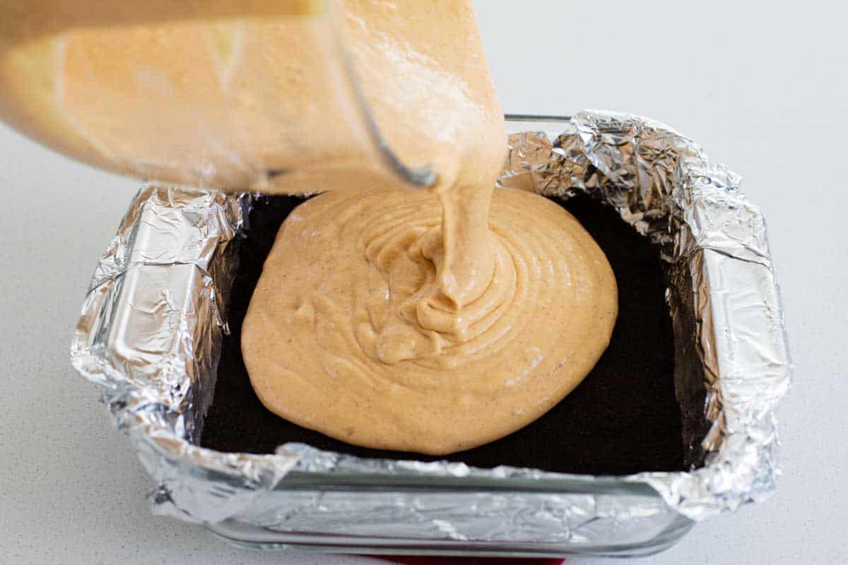 pouring cheesecake batter over a chocolate cookie crust