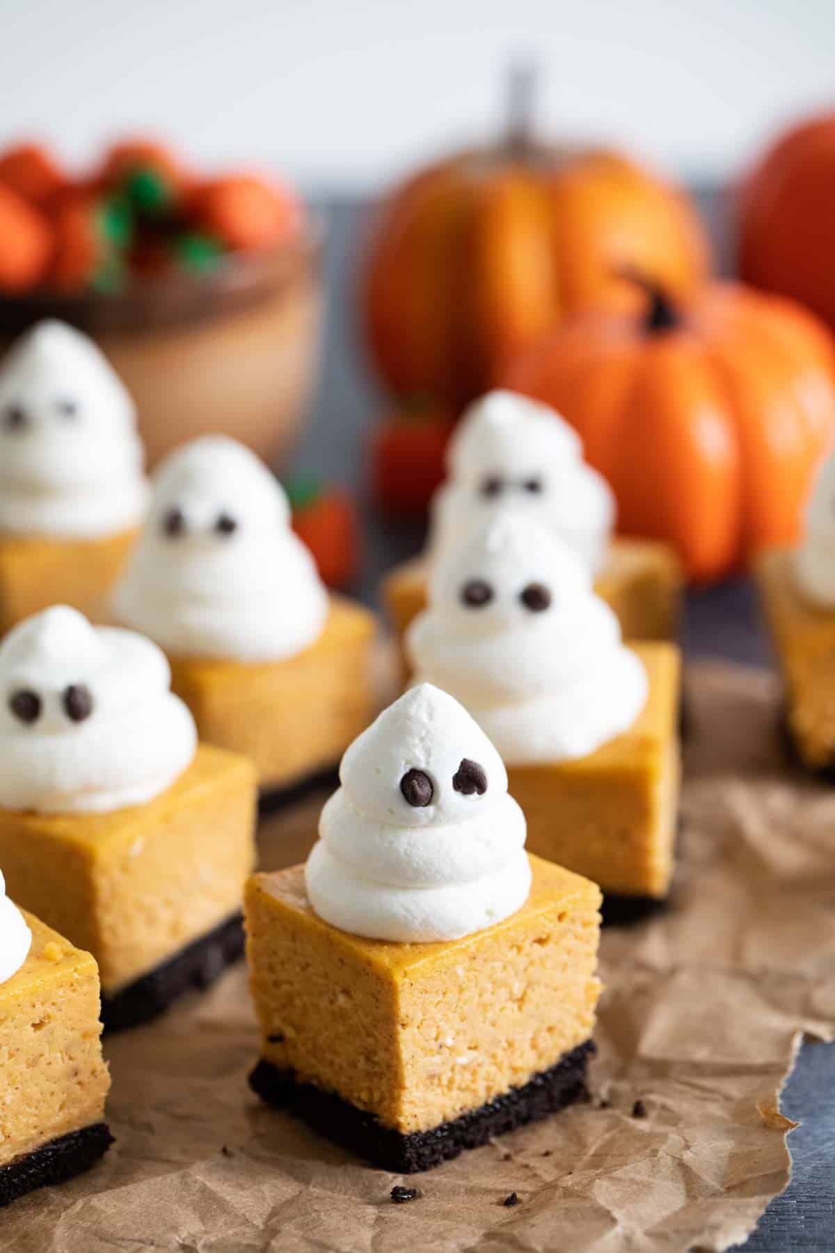 Pumpkin cheesecake bars topped with whipped cream ghosts.