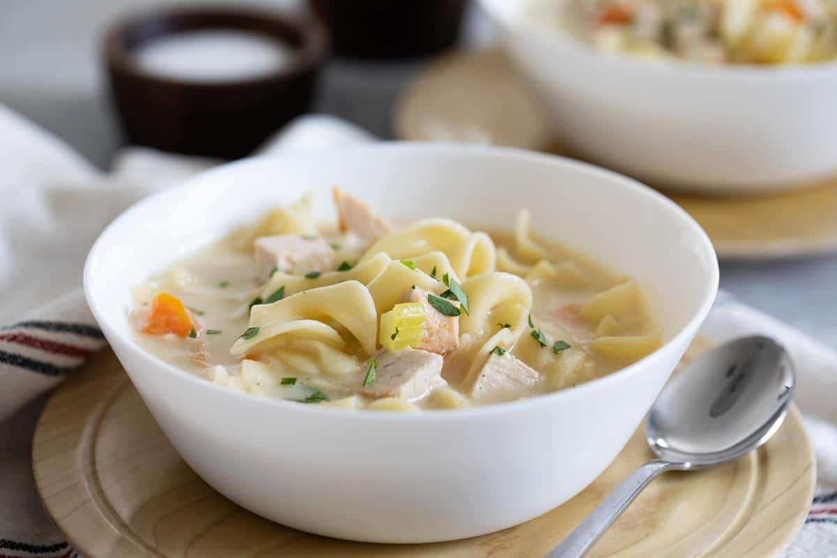 The perfect soup for leftovers, this Creamy Turkey Noodle Soup is ideal for leftover Thanksgiving turkey, but is a great way to use up leftover chicken, as well! bowl of Creamy Turkey Noodle Soup with a spoon on the side