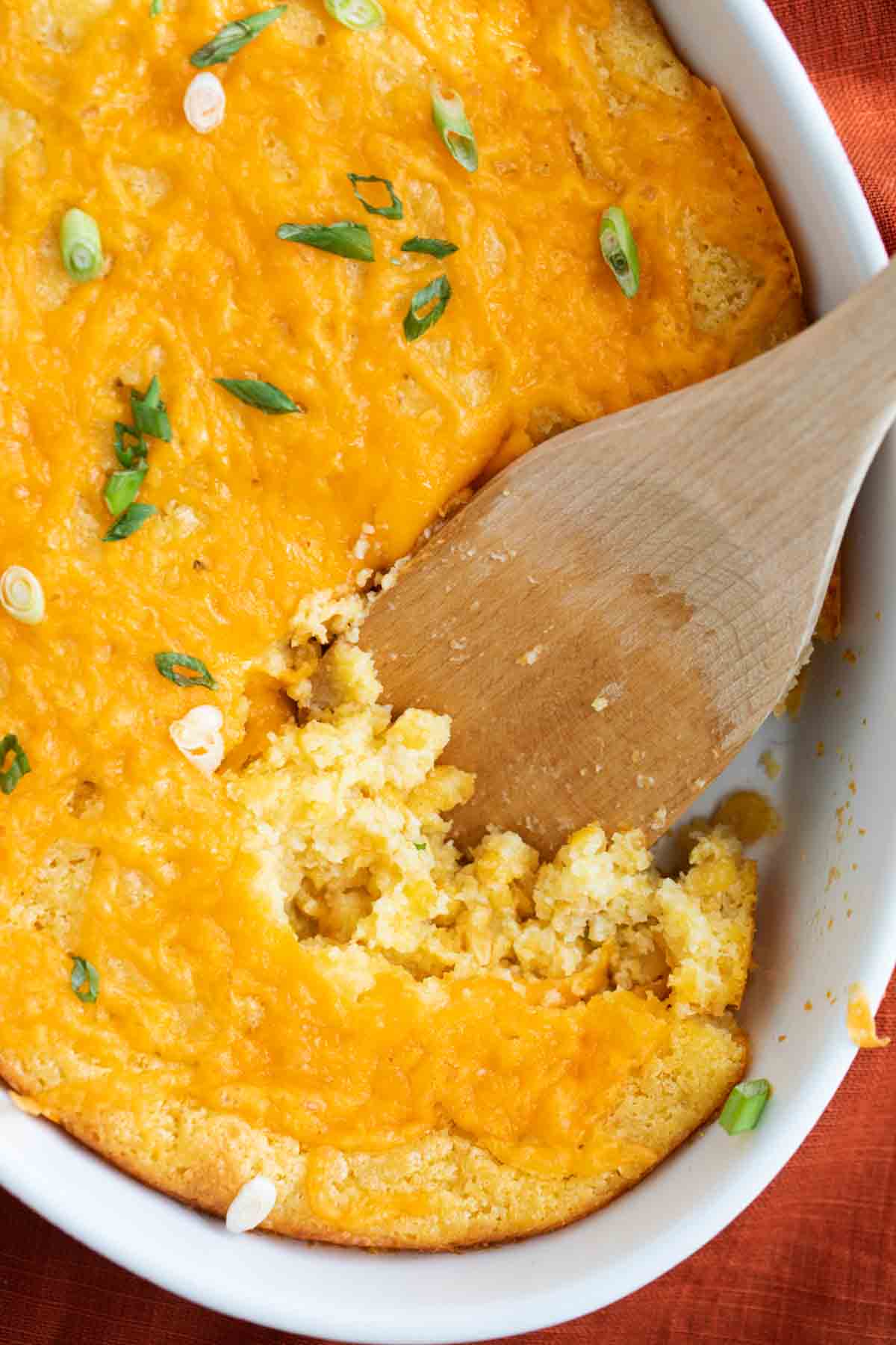 overhead view of corn casserole in a dish with a wooden spoon