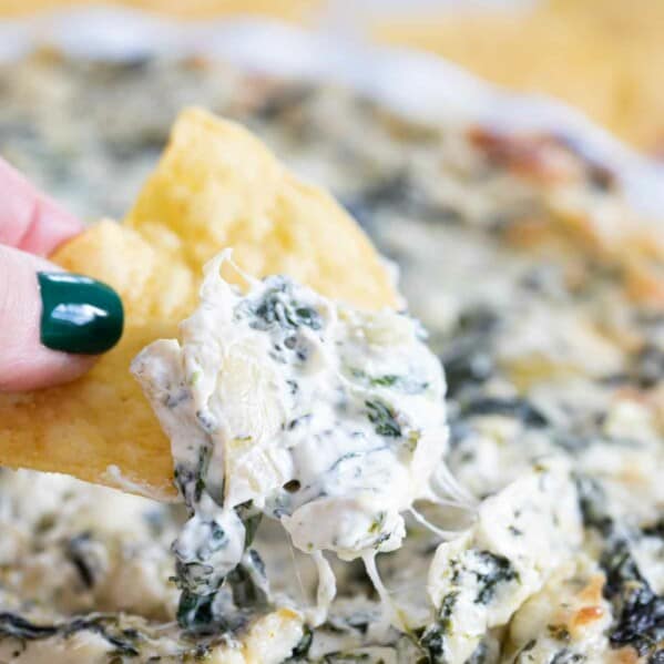 scooping spinach artichoke dip on a tortilla chip
