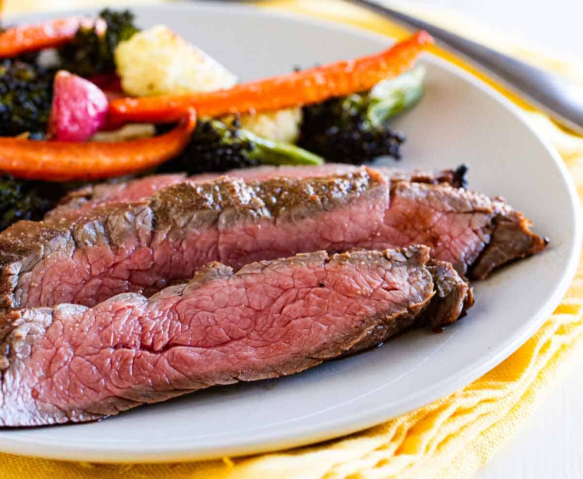 sliced grilled flank steak on a plate with vegetables