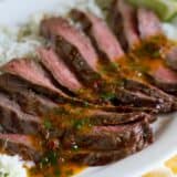 sliced flank steak with chipotle butter over rice on a platter