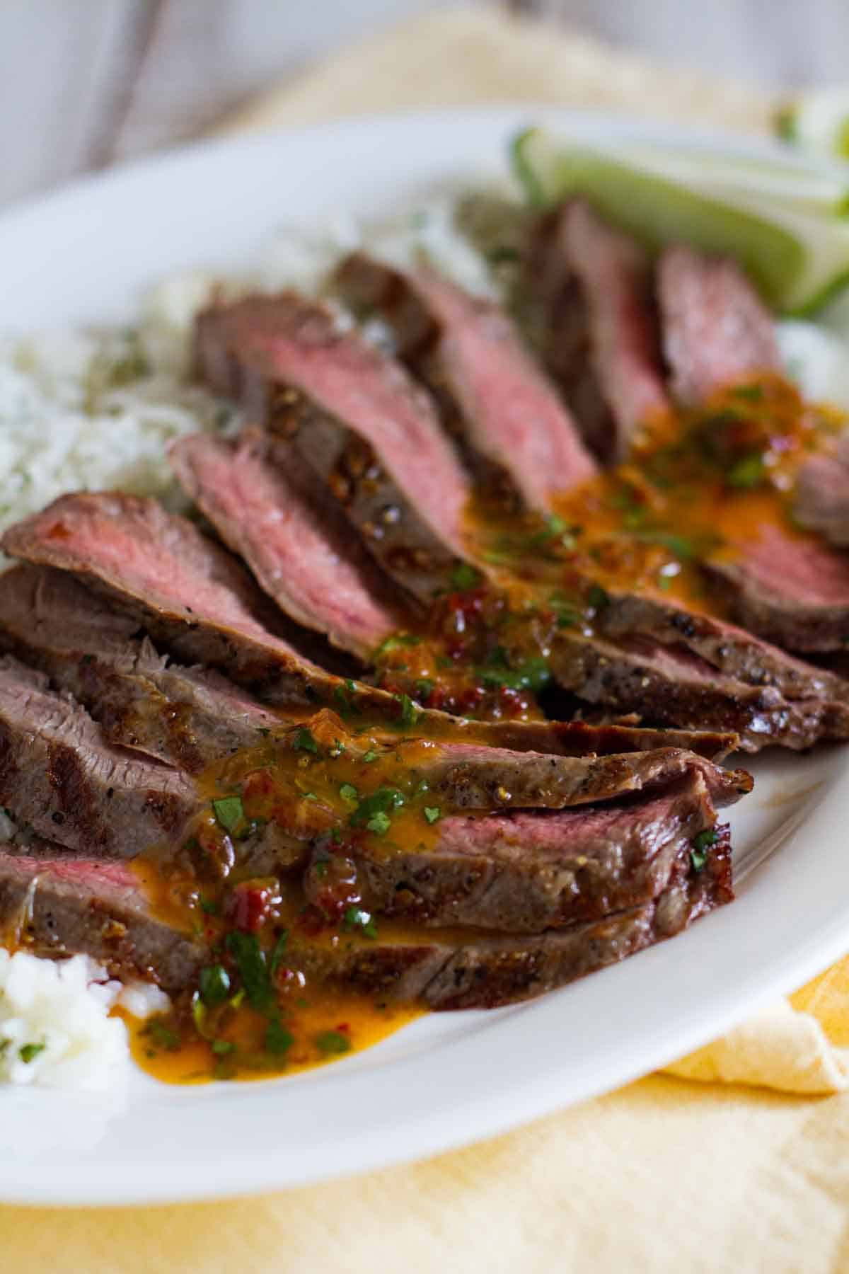 sliced flank steak with chipotle butter over rice on a platter