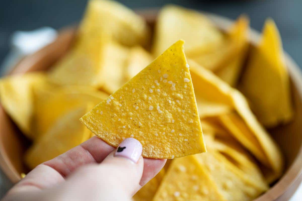 single tortilla chip with bowl of tortilla chips behind