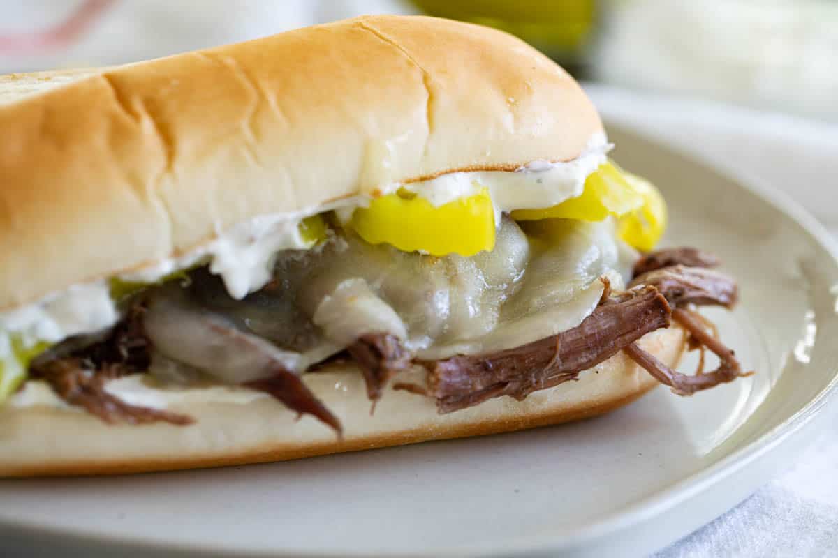 Italian beef sandwich with pepperoncini peppers and melted cheese on a plate