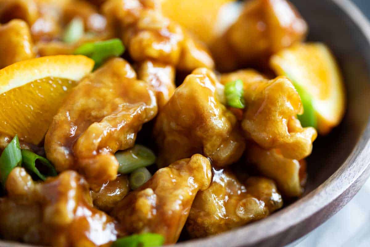 Better than take-out, this Orange Chicken Recipe is easy to make at home. It is full of flavor and will have you wanting more! close up of orange chicken with pieces of orange and green onion