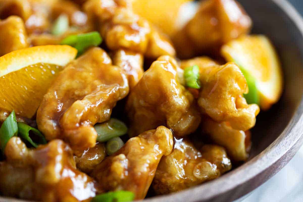 close up of orange chicken with pieces of orange and green onion