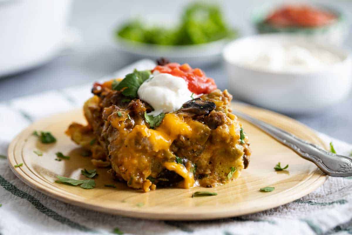 Filled with sausage, mushrooms and green chiles, this Sausage Breakfast Casserole is hearty and filling. Plus, all of the work is done the night before, which makes breakfast a snap! wooden plate with a slice of Sausage Breakfast Casserole topped with sour cream