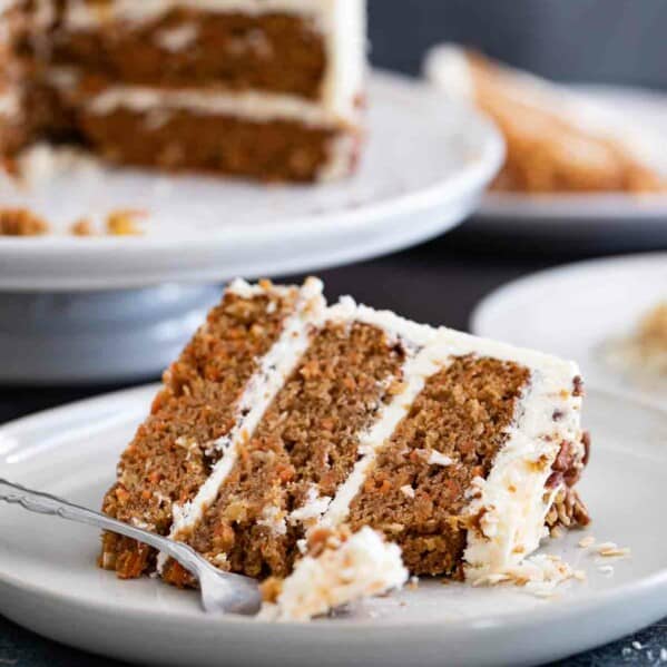 slice of carrot cake with a full carrot cake behind