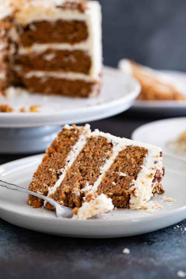 slice of carrot cake with a full carrot cake behind