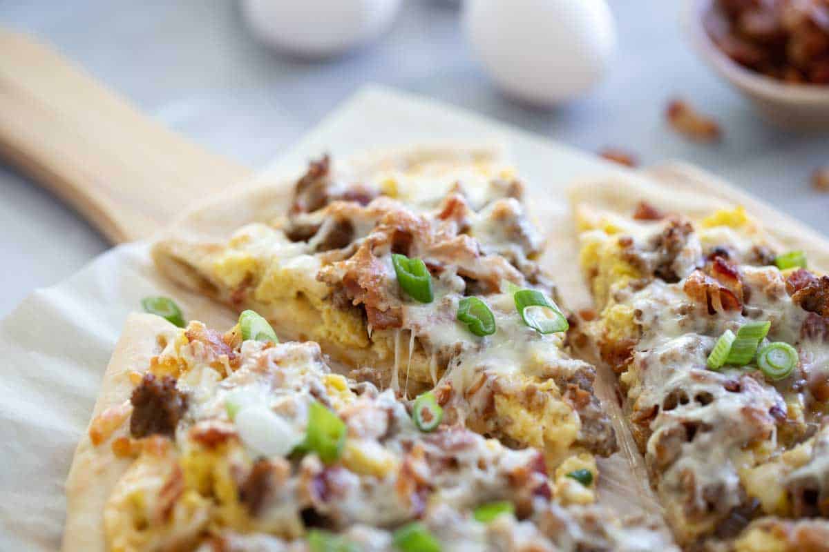 Perfect for breakfast or dinner, this Breakfast Pizza is topped with sausage, bacon, eggs, and an easy cheese sauce. This is a great way to do something different for pizza night! sliced breakfast pizza on parchment paper