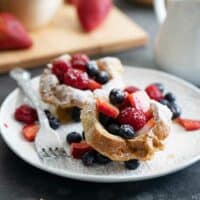 two french toast cups on a plate with fresh berries and powdered sugar