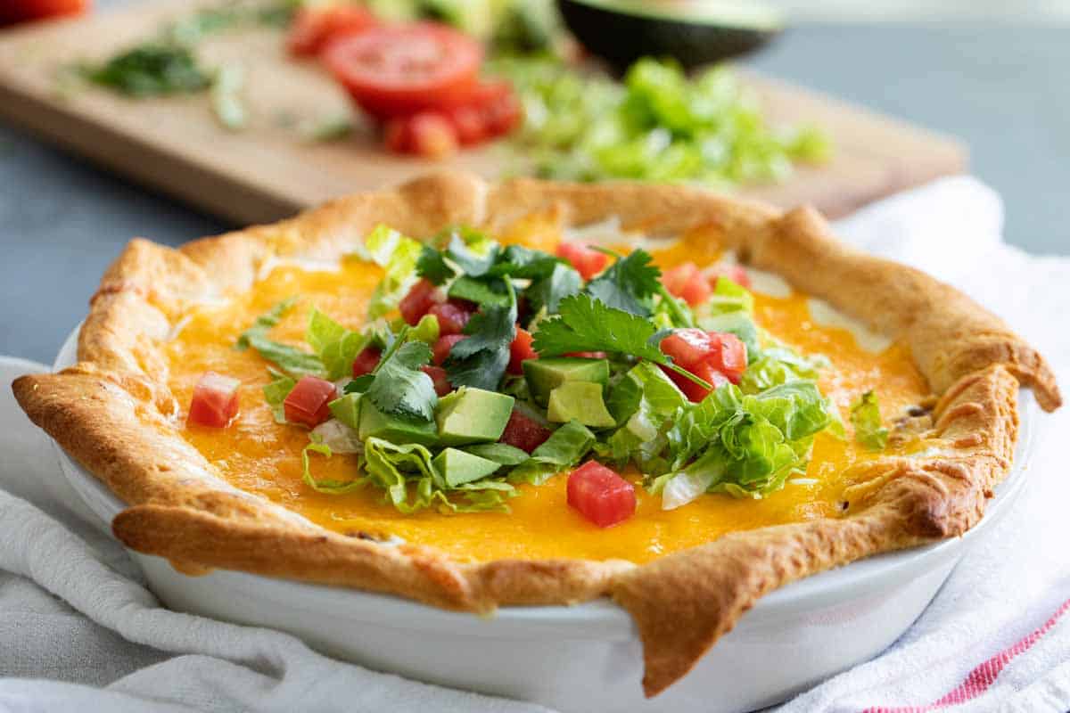 This Taco Pie is an easy taco inspired dish with a crescent roll crust and ground beef filling that is topped with crushed tortilla chips, sour cream and cheese. whole taco pie made with crescent rolls with toppings on top