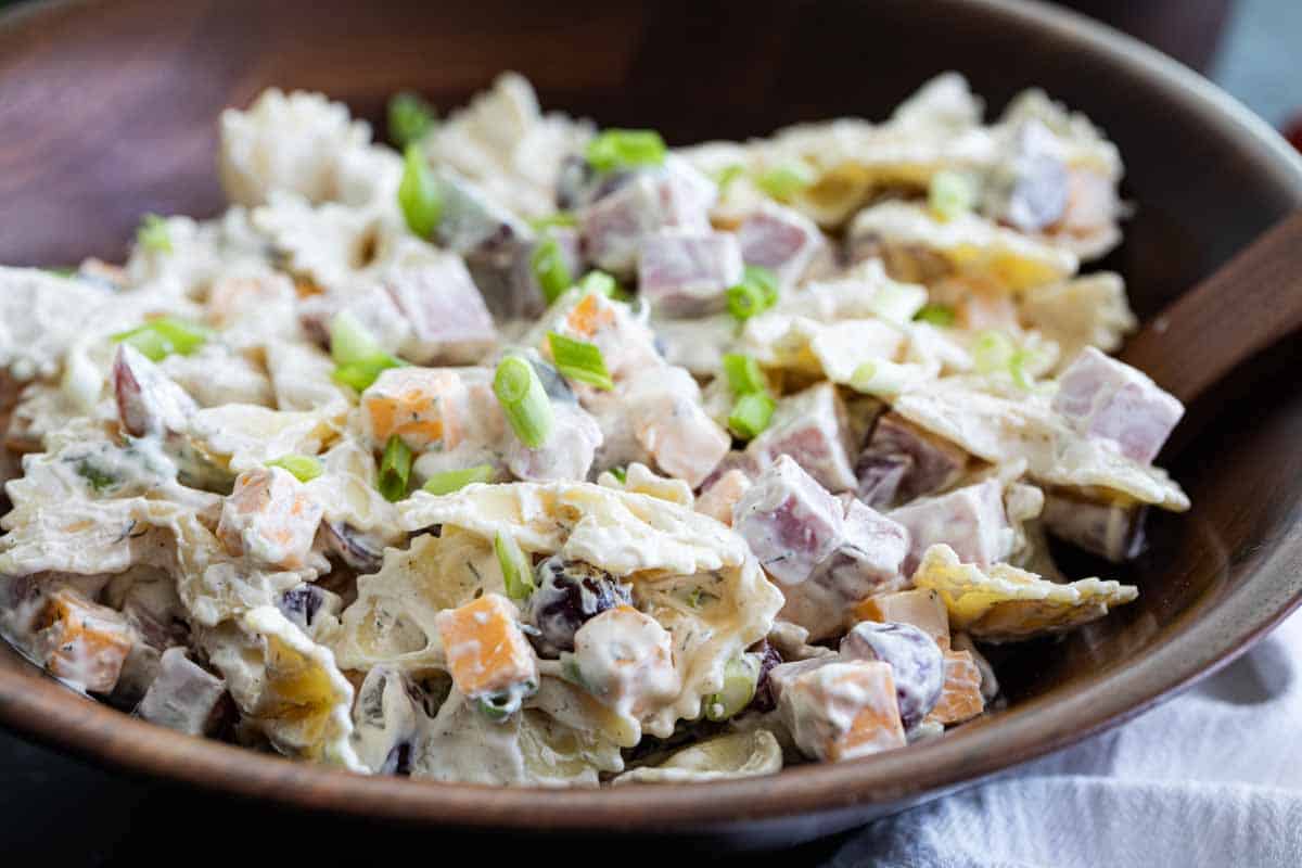 Looking for the best pasta salad recipe? This Bow Tie Pasta Salad is a little bit different than your typical pasta salad recipe, and a salad you’ll want to make year after year! wooden bowl filled with bow tie pasta salad with creamy dressing