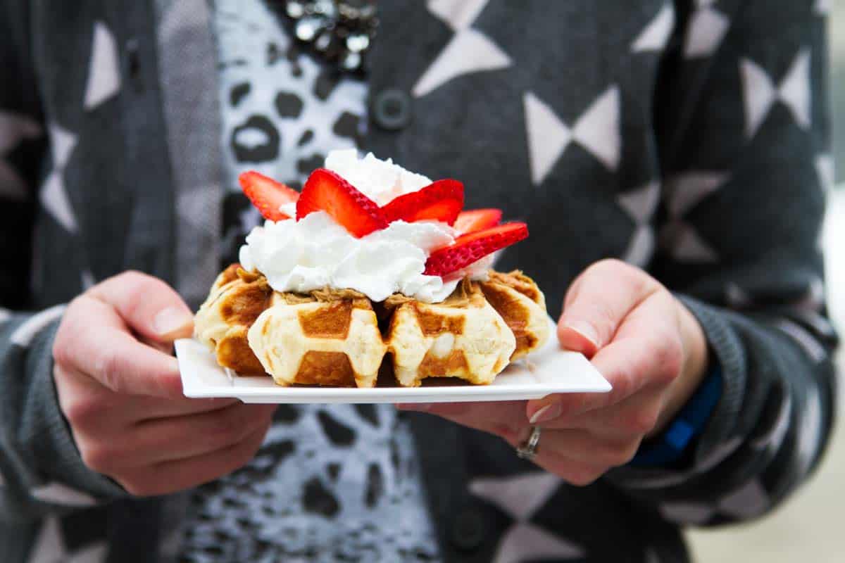 holding a plate with a liege waffle topped with whipped cream and strawberries