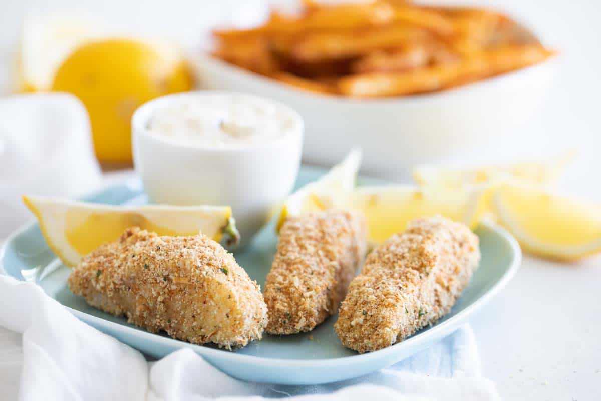 homemade fish sticks on a blue plate with lemons