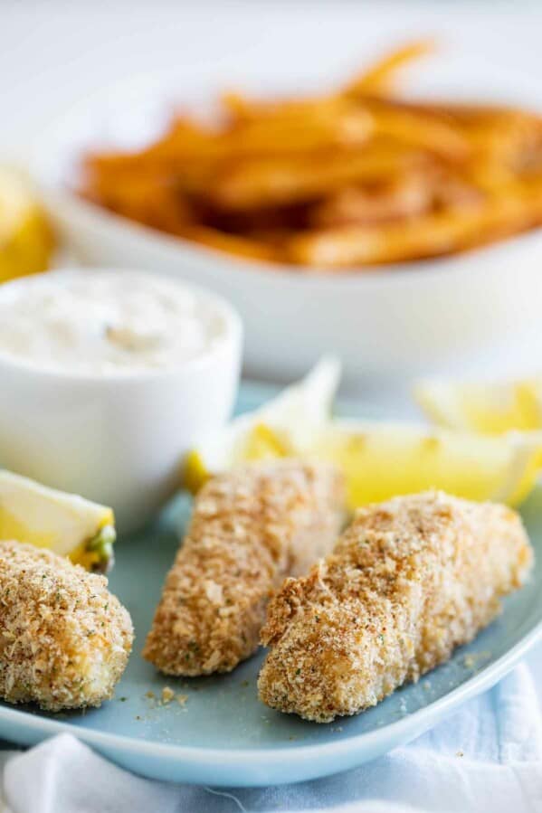Homemade fish sticks on a plate with fries in the background