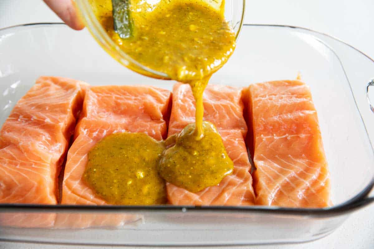 pouring honey mustard over salmon in a baking dish