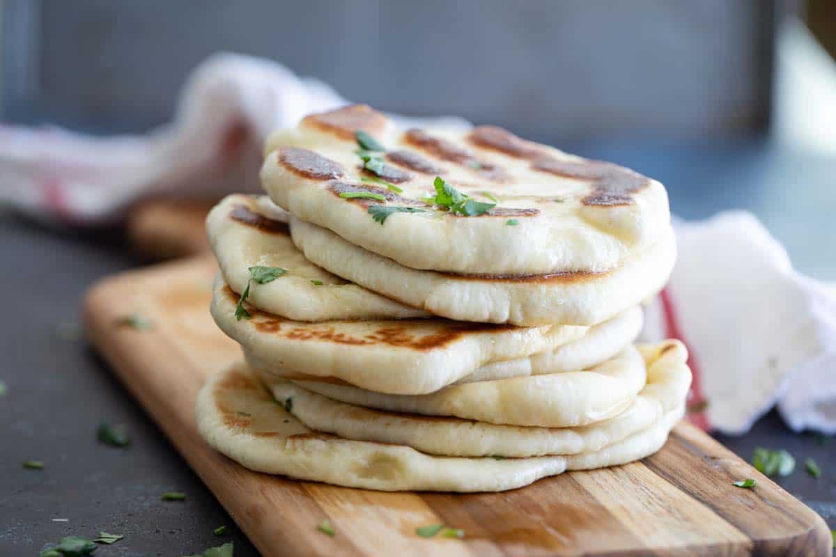 a stack of naan bread on a cutting board sprinkled with cilantro