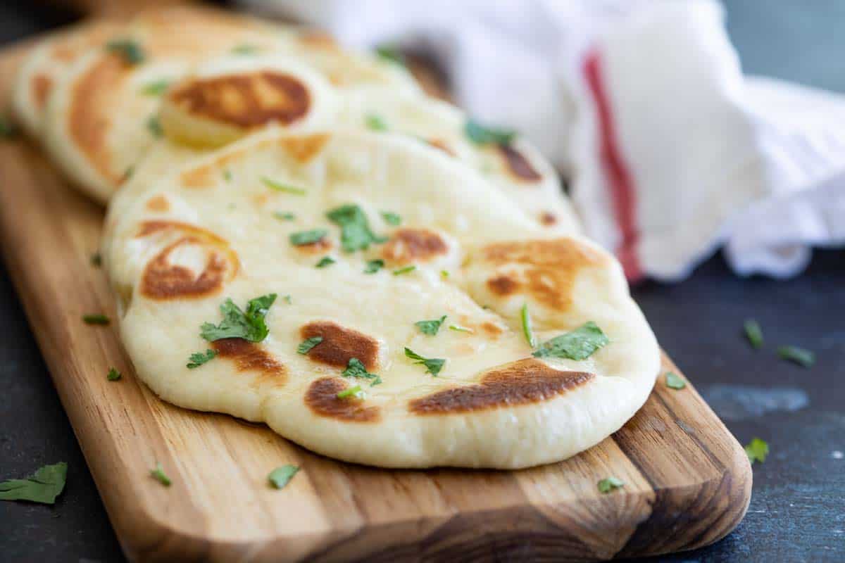 homemade naan bread sprinkled with cilantro on a cutting board