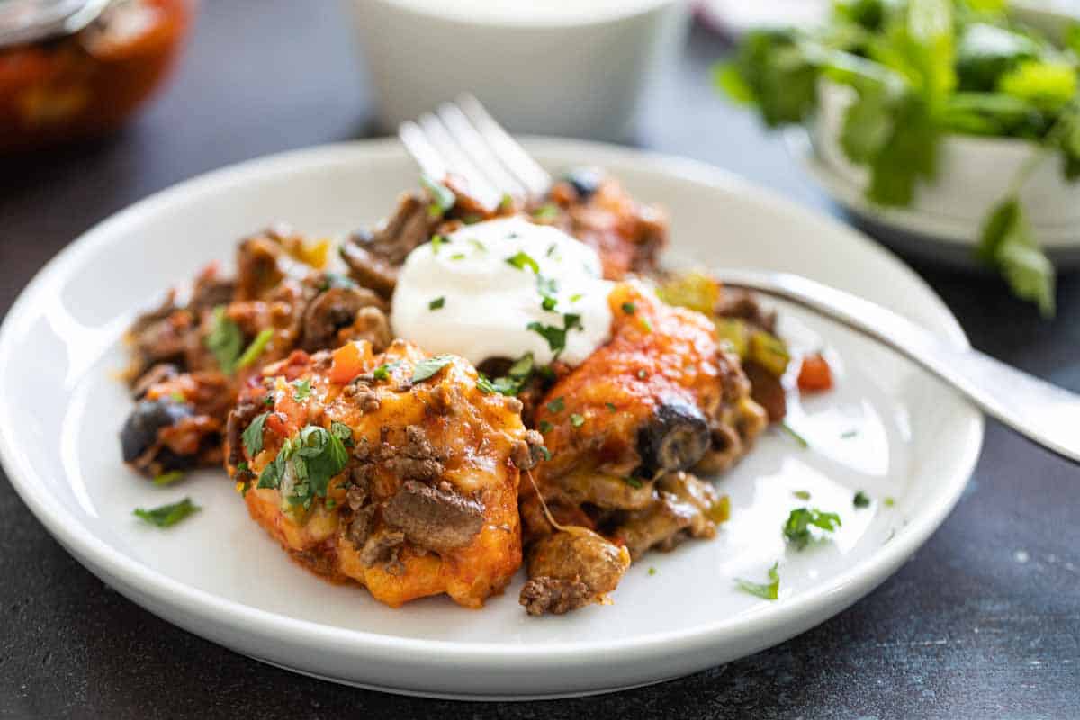 Biscuits are coated in taco sauce then topped with spiced ground beef and lots of cheese in this family friendly Taco Casserole. taco casserole on a white plate with a fork