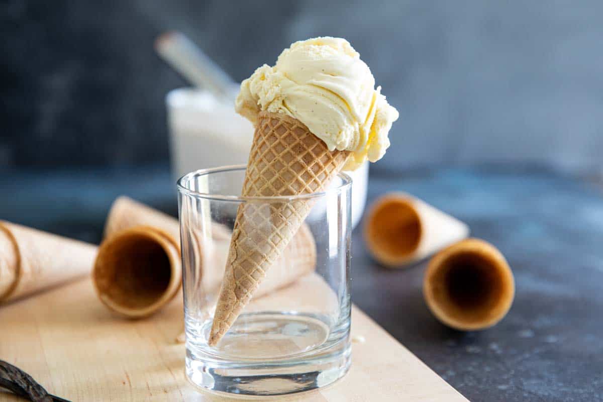 You can’t go wrong with a classic! This Vanilla Ice Cream recipe is a custard based ice cream recipe with real vanilla bean flecks and lots of vanilla flavor throughout. vanilla ice cream on a cone sitting up in a cup