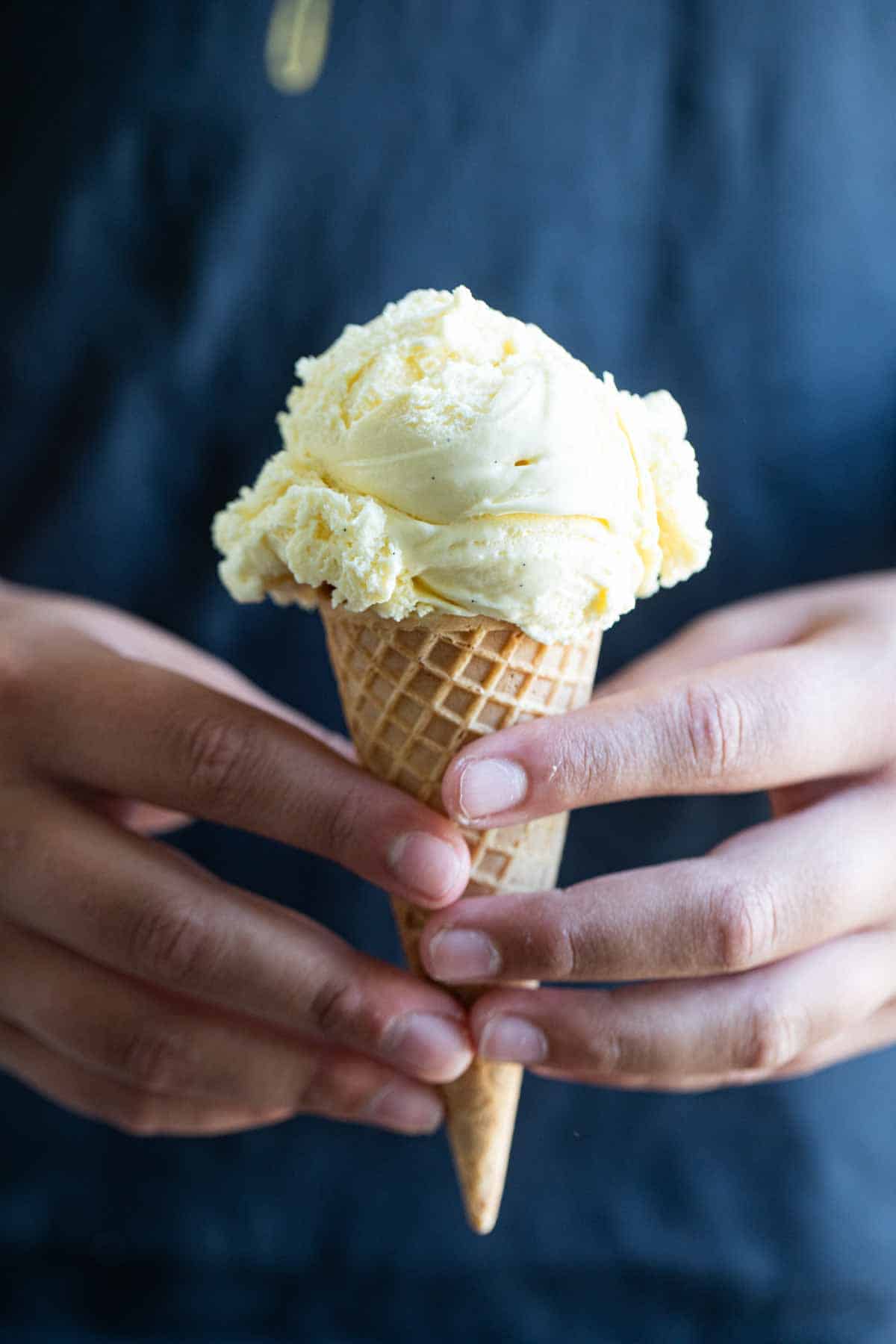 hands holding a scoop of ice cream in a sugar cone