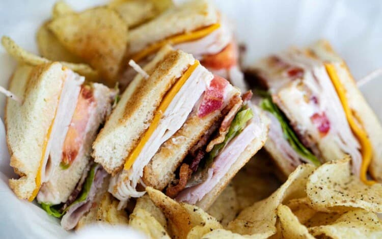 pieces of club sandwich in a basket with potato chips