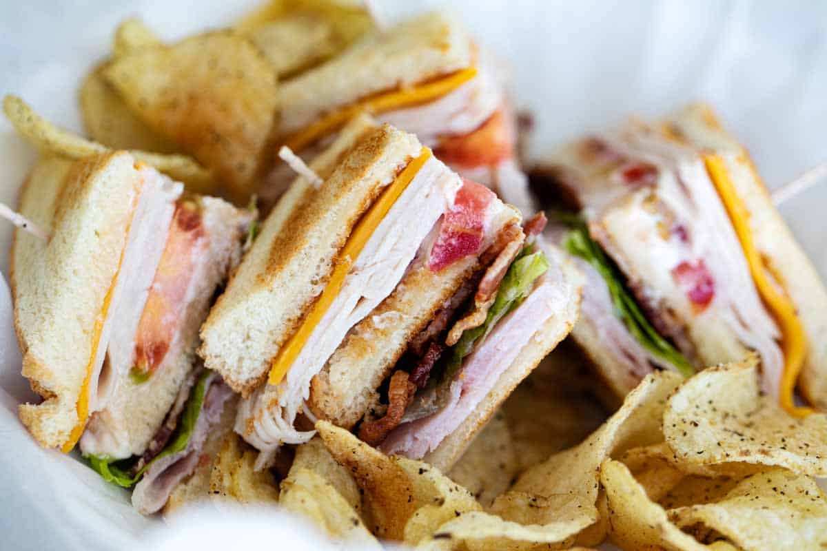 pieces of club sandwich in a basket with potato chips