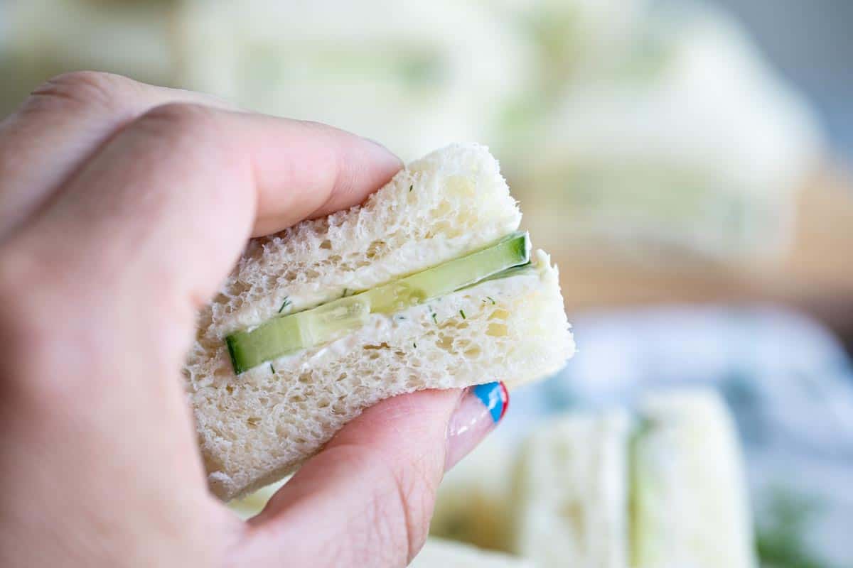 holding a finger sandwich with cucumbers