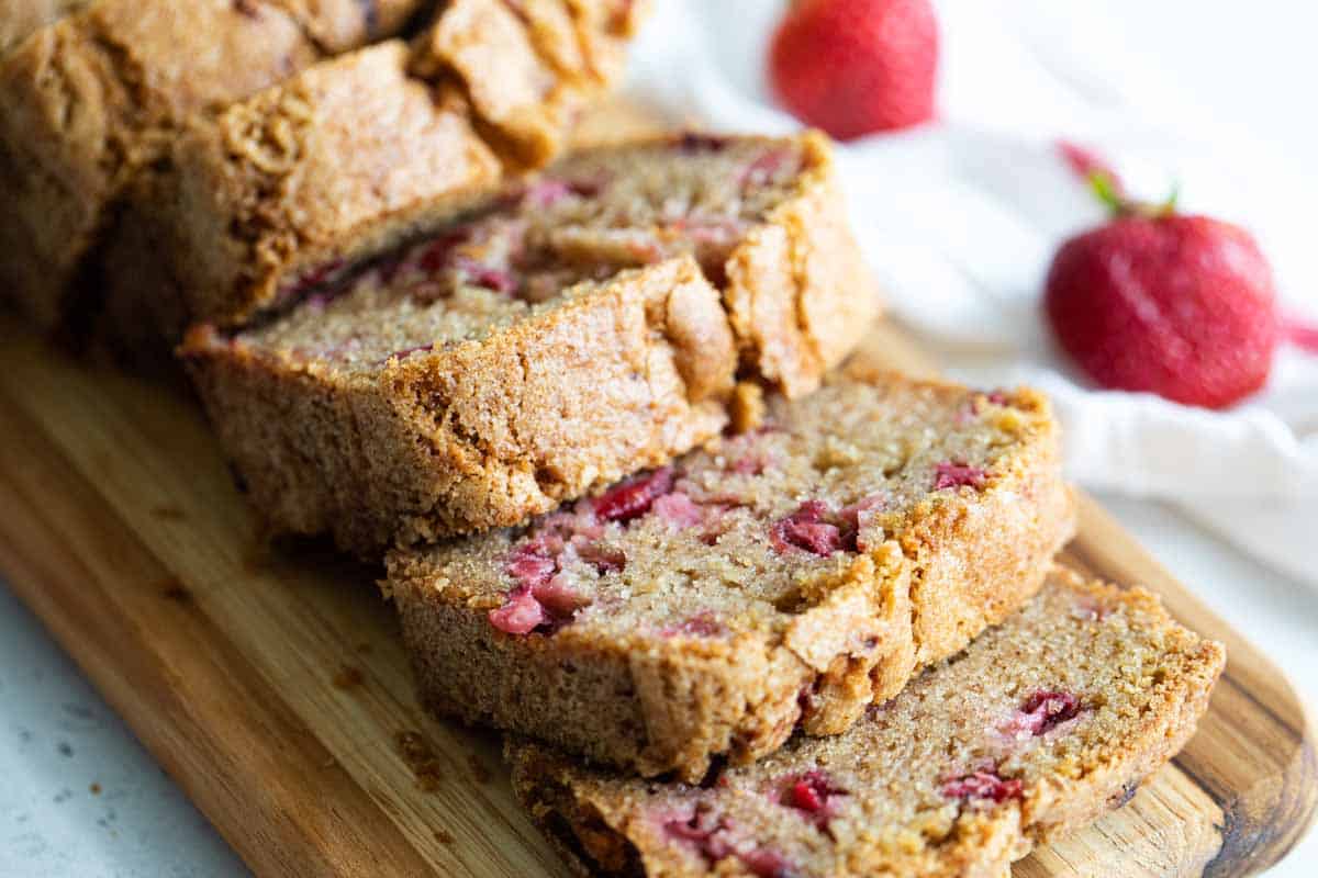 Fresh strawberries and cinnamon are the stars in this easy Strawberry Bread. A great way to take advantage of strawberry season! loaf of sliced strawberry bread with fresh strawberries behind.